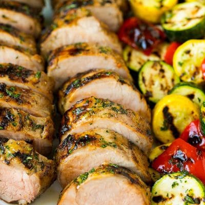Grilled pork tenderloin on a serving plate with grilled vegetables on the side.