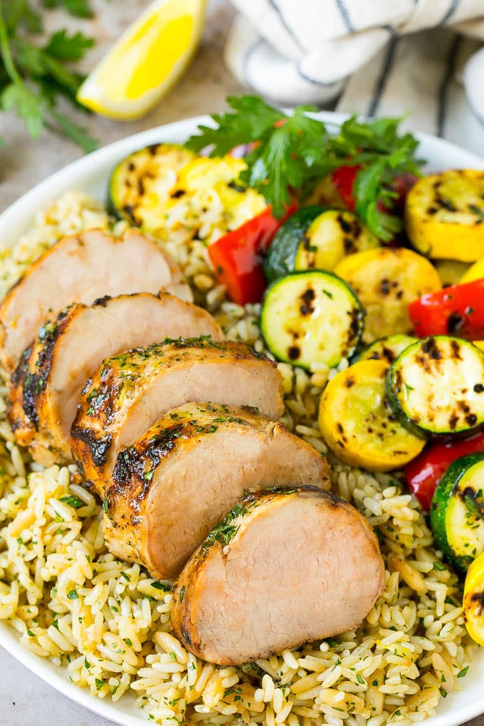 Sliced pork tenderloin on a plate of couscous with vegetables.