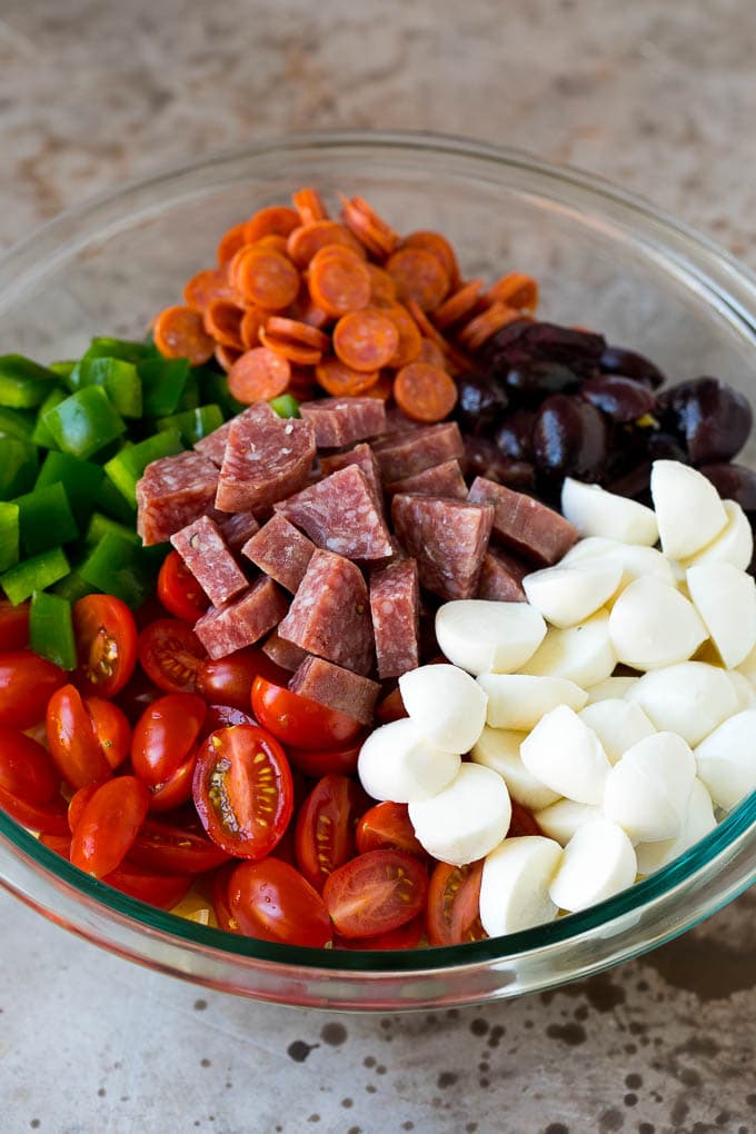 A bowl of pasta, mozzarella balls, cherry tomatoes, bell peppers and olives.