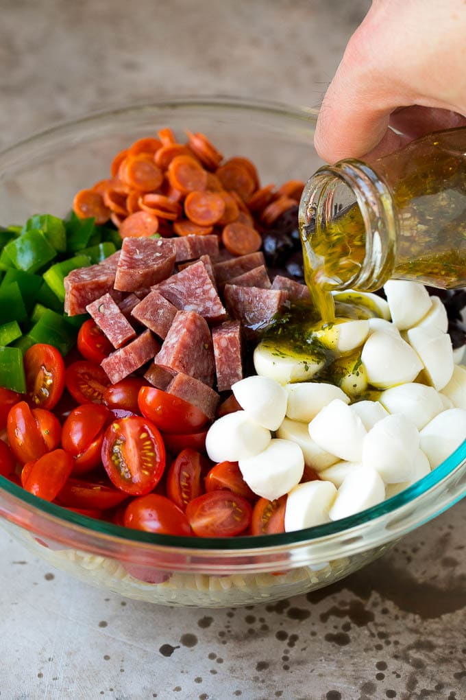 Italian dressing being poured over pasta salad ingredients.