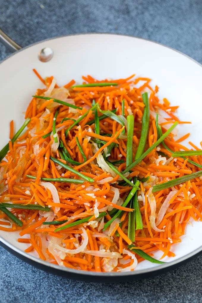 Cooked carrots and green onions in a pan.