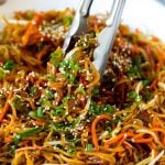 Tongs serving up a portion of pan fried noodles with vegetables.