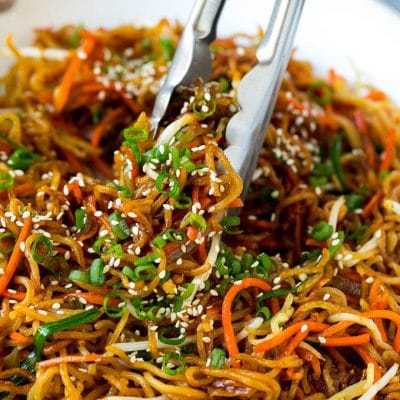 Tongs serving up a portion of pan fried noodles with vegetables.