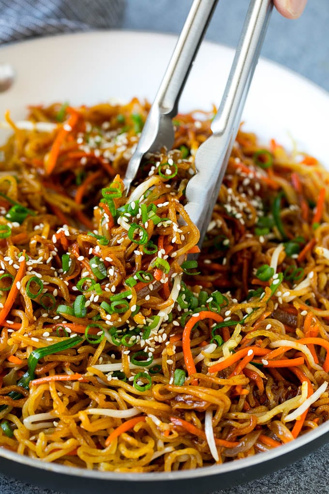 Tongs serving up a portion of pan fried noodles with vegetables.