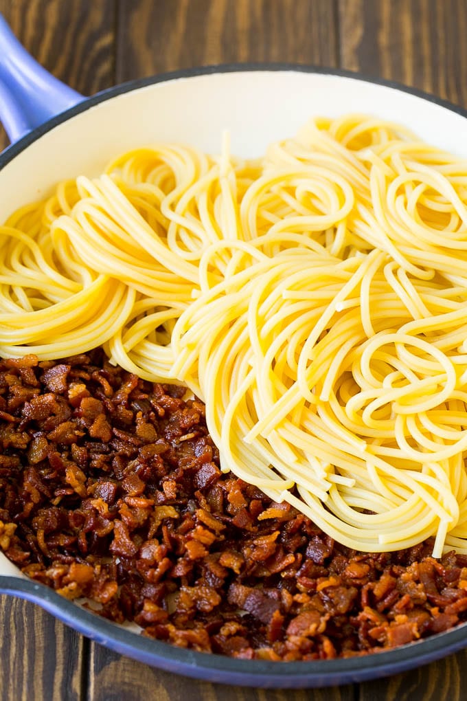 Cooked bacon and spaghetti in a skillet.