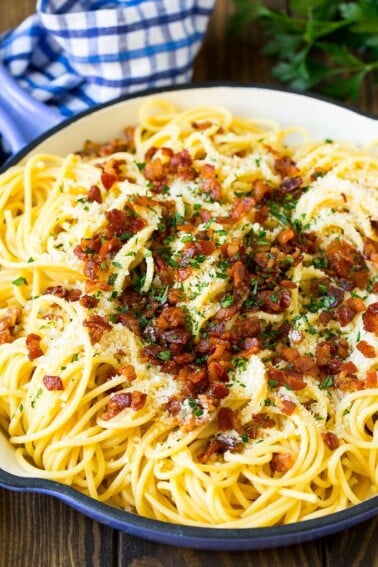 A skillet of pasta carbonara topped with bacon, parmesan cheese and parsley.