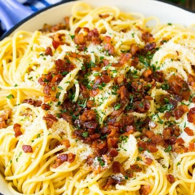 A skillet of pasta carbonara topped with bacon, parmesan cheese and parsley.