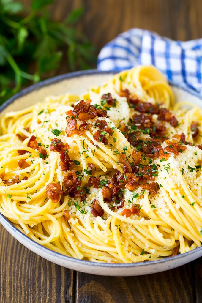 A bowl of carbonara pasta topped with bacon and cheese.