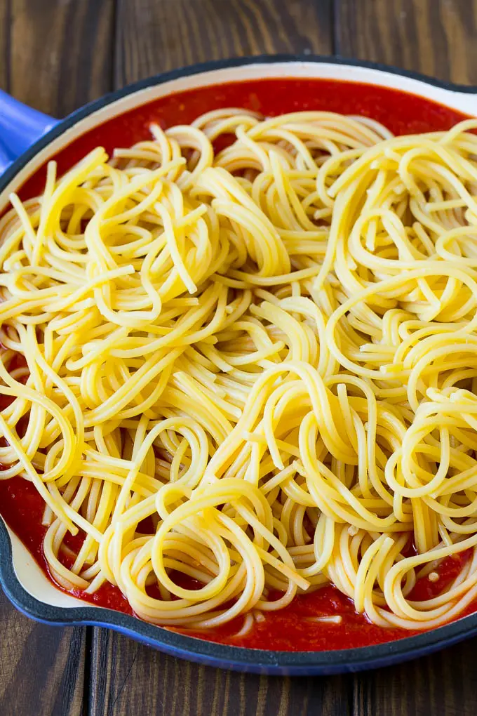 Spaghetti noodles in a pan of tomato sauce.