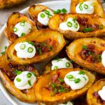A plate of potato skins topped with bacon, cheese, sour cream and green onions.