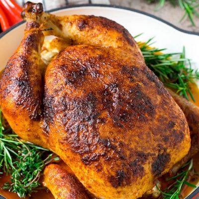 A rotisserie chicken in a red skillet with sprigs of fresh herbs.