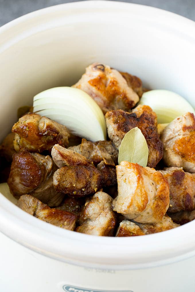 Pork, onions, spices and bay leaves in a slow cooker.