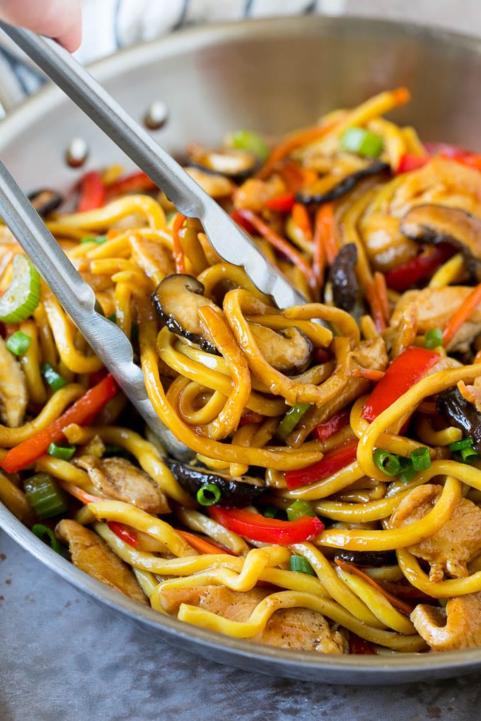 Tongs serving up a portion of chicken and noodle stir fry.