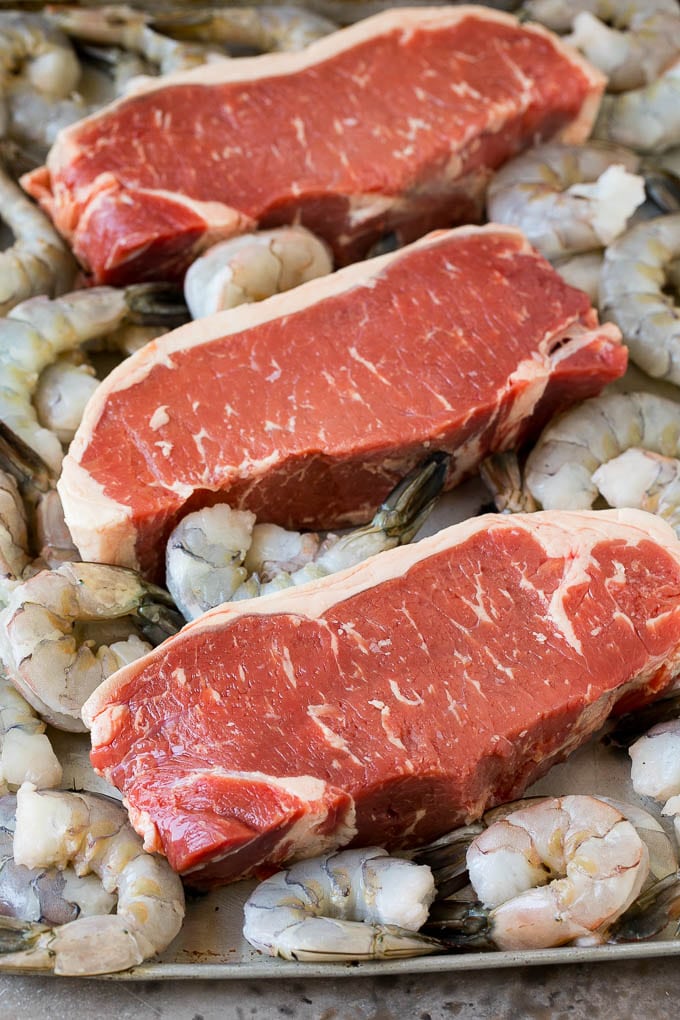 Raw steaks and shrimp on a sheet pan.