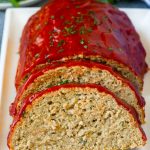 A sliced turkey meatloaf topped with ketchup and chopped parsley.