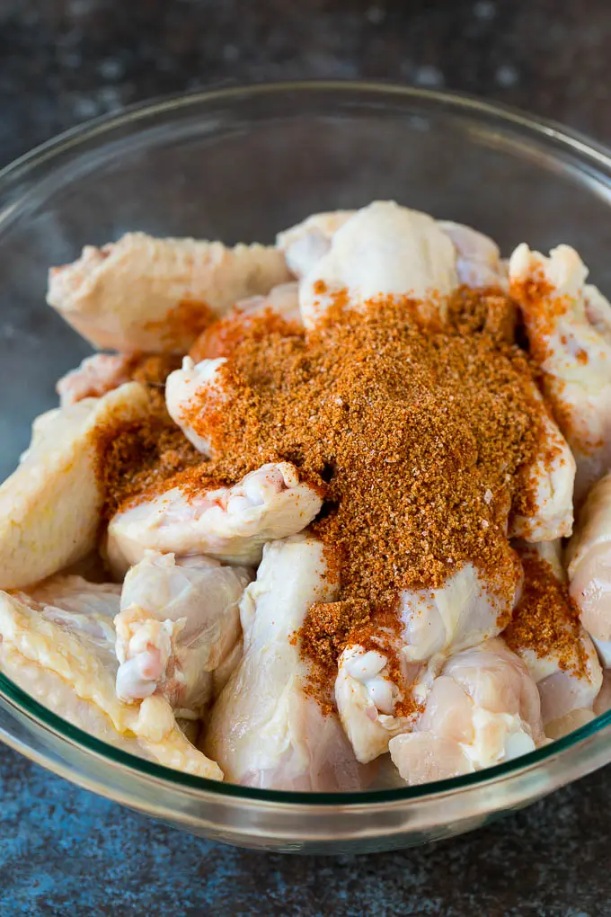 Chicken wings and spice rub in a mixing bowl.