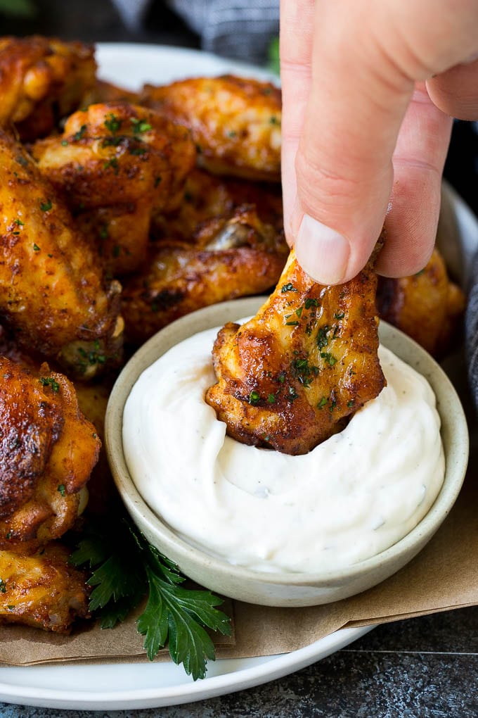 A chicken wing being dipped into ranch sauce.