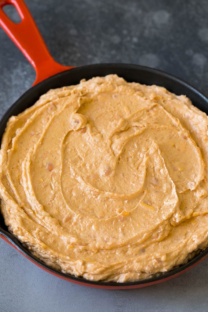 Refried frijoles mixed with cream cheese, sour cream and seasonings in a skillet.