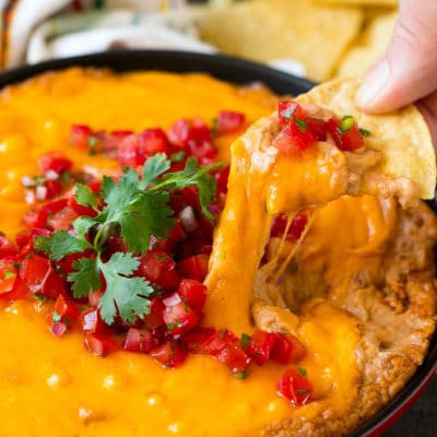 A tortilla chip scooping out a serving of Mexican bean dip.