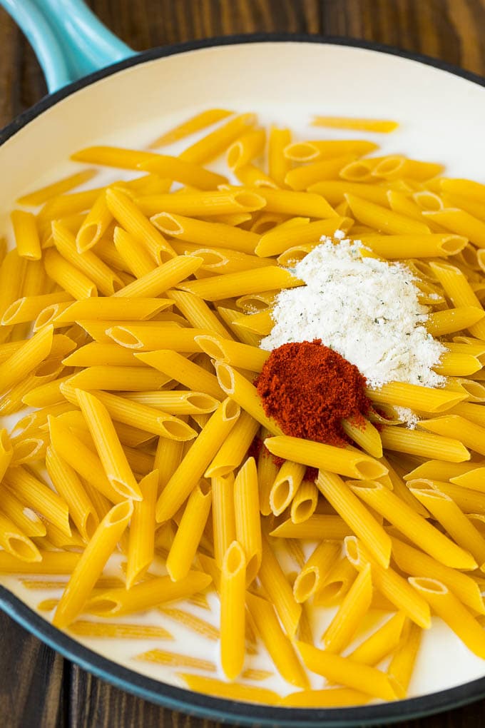 Penne pasta with seasonings in a pan of milk.