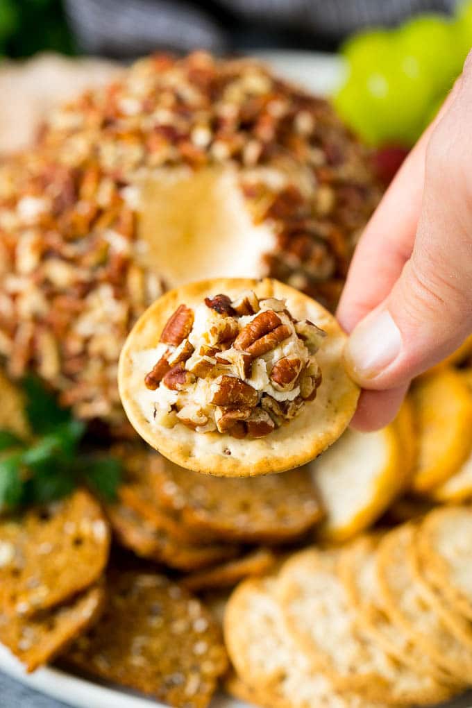 A hand holding a cracker topped with cheese spread.