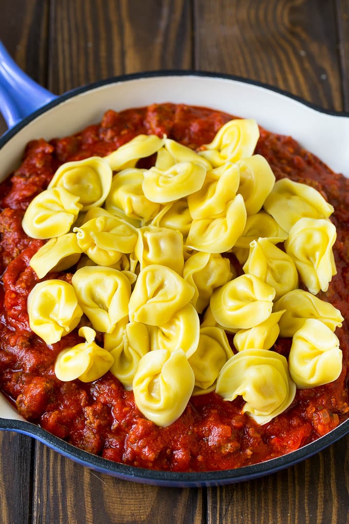 Cooked tortellini over meat sauce in a skillet.