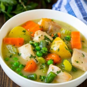 A bowl of chicken stew with celery, potatoes, green beans and peas.