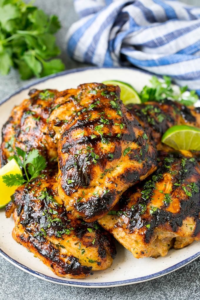 Grilled chicken thighs with a garnish of cilantro and lime wedges.