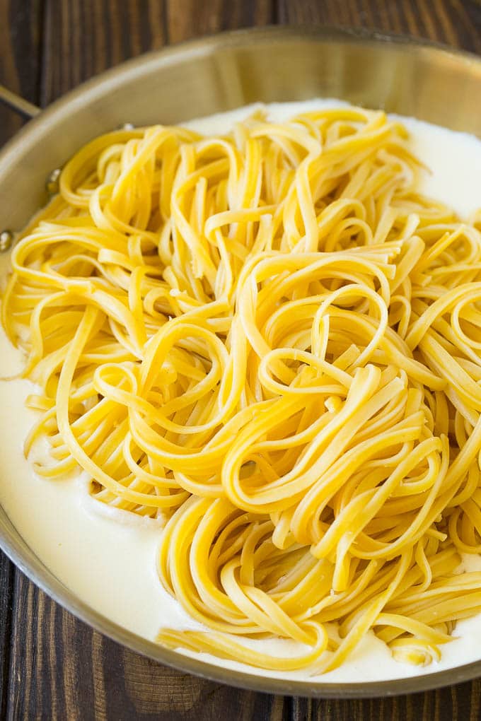 Linguine pasta in a pan of cream sauce.