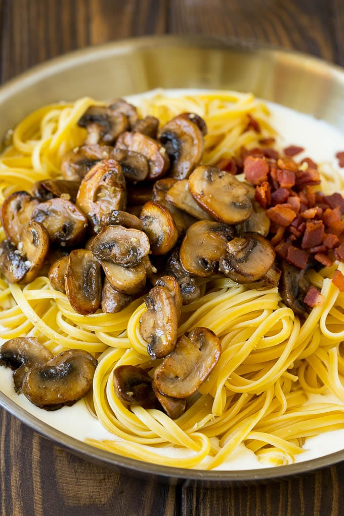 A pan of cream sauce with pasta, bacon and mushrooms.