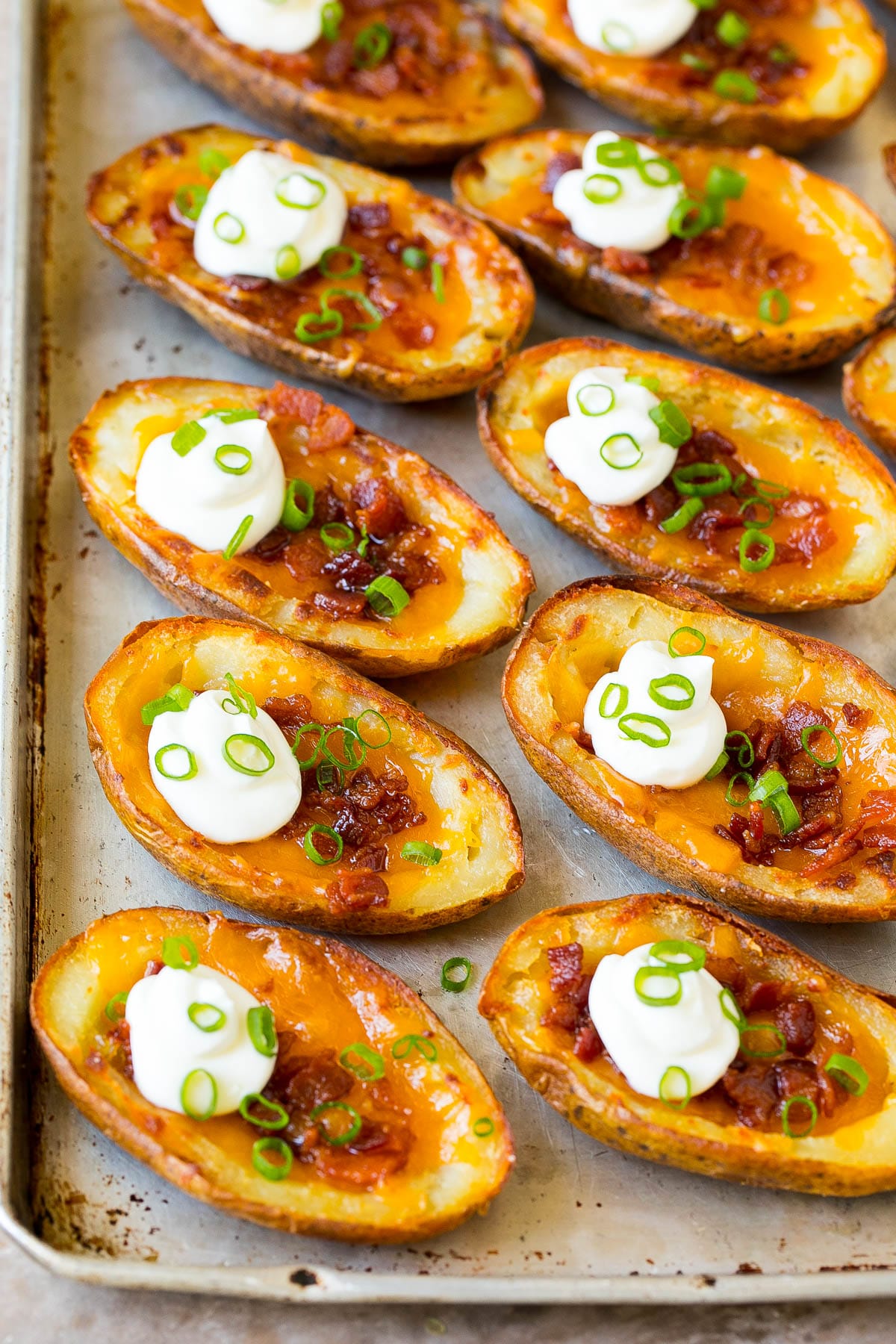 A sheet pan filled with potato skins that are topped with sour cream and green onions.