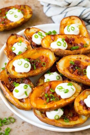 A serving plate of potato skins topped with bacon and sour cream.