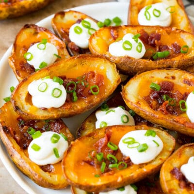 A serving plate of potato skins topped with bacon and sour cream.