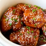 Slow cooker chicken thighs garnished with sesame seeds and green onions.