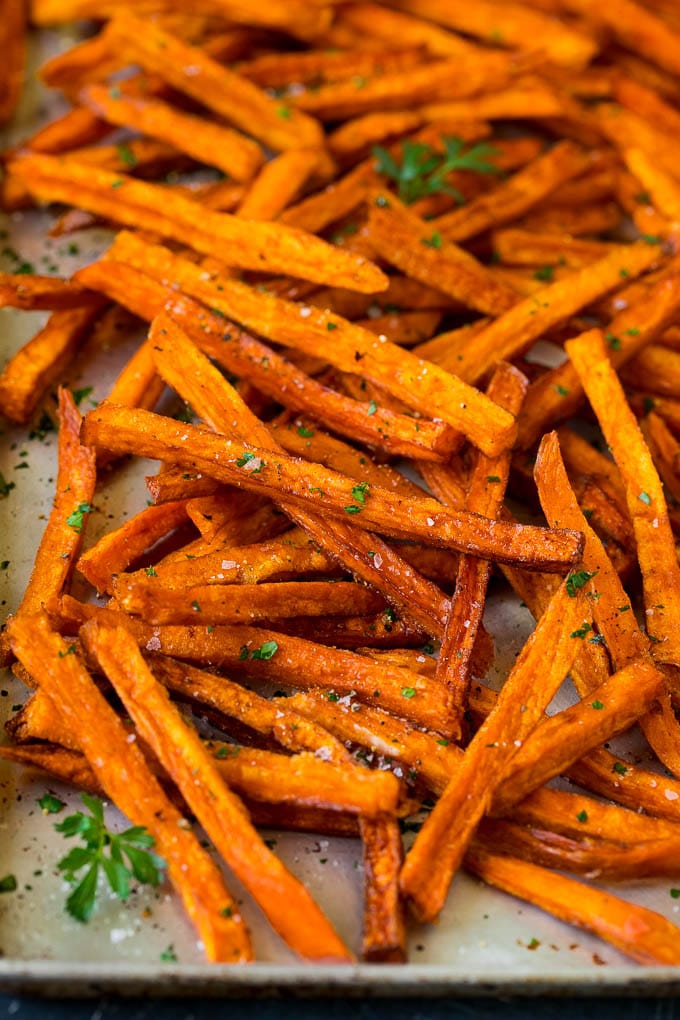 Sweet potato fries on a sheet pan, topped with salt, pepper and parsley.