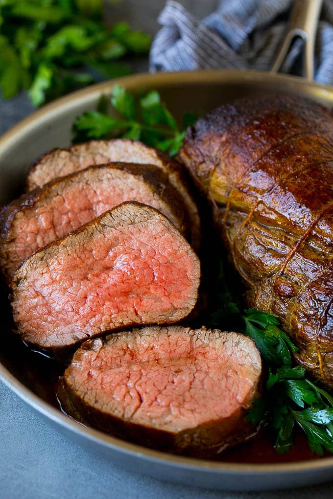 A sliced beef tenderloin recipe in a pan, garnished with fresh parsley.