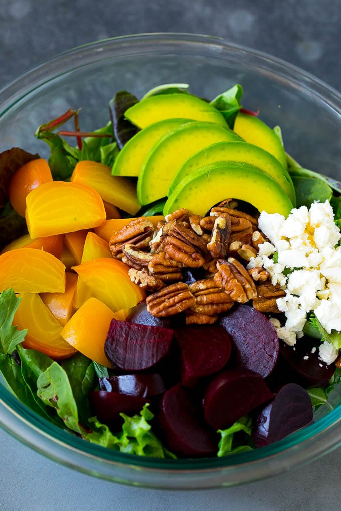 Red and yellow beets, salad greens, feta cheese, avocado and pecans in a bowl.