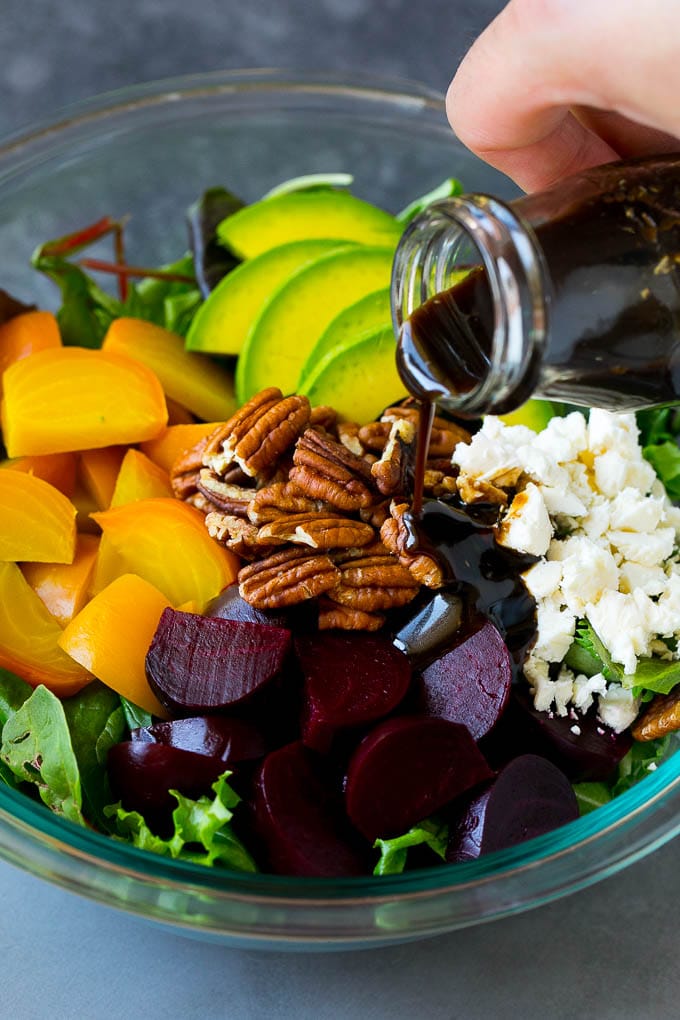 Balsamic dressing being poured over beets, sliced avocado and feta cheese.