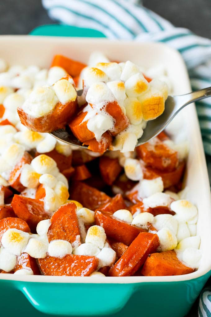 A spoon serving up a portion of candied yams topped with marshmallows.