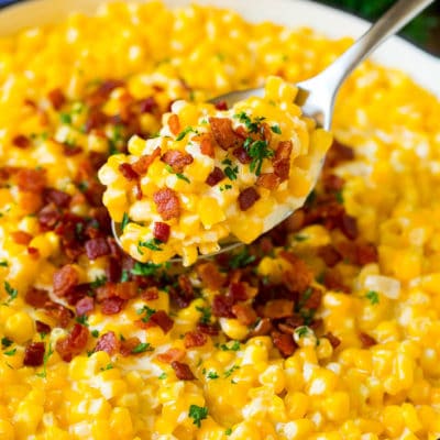 A spoonful of creamed corn topped with bacon and fresh herbs.