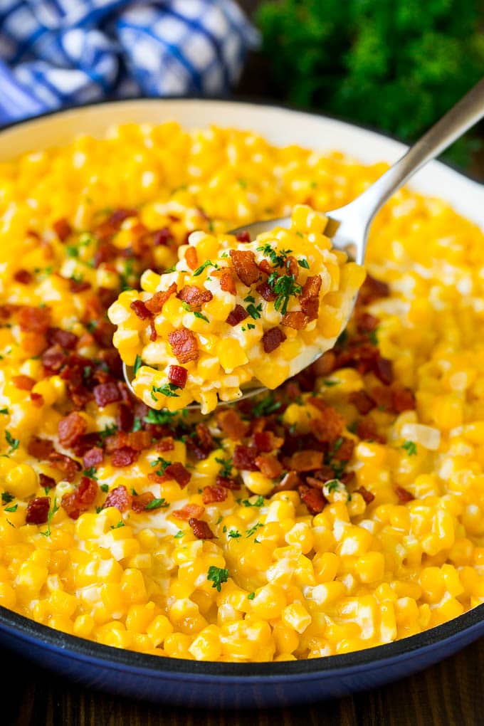 A spoonful of creamed corn topped with bacon and fresh herbs.
