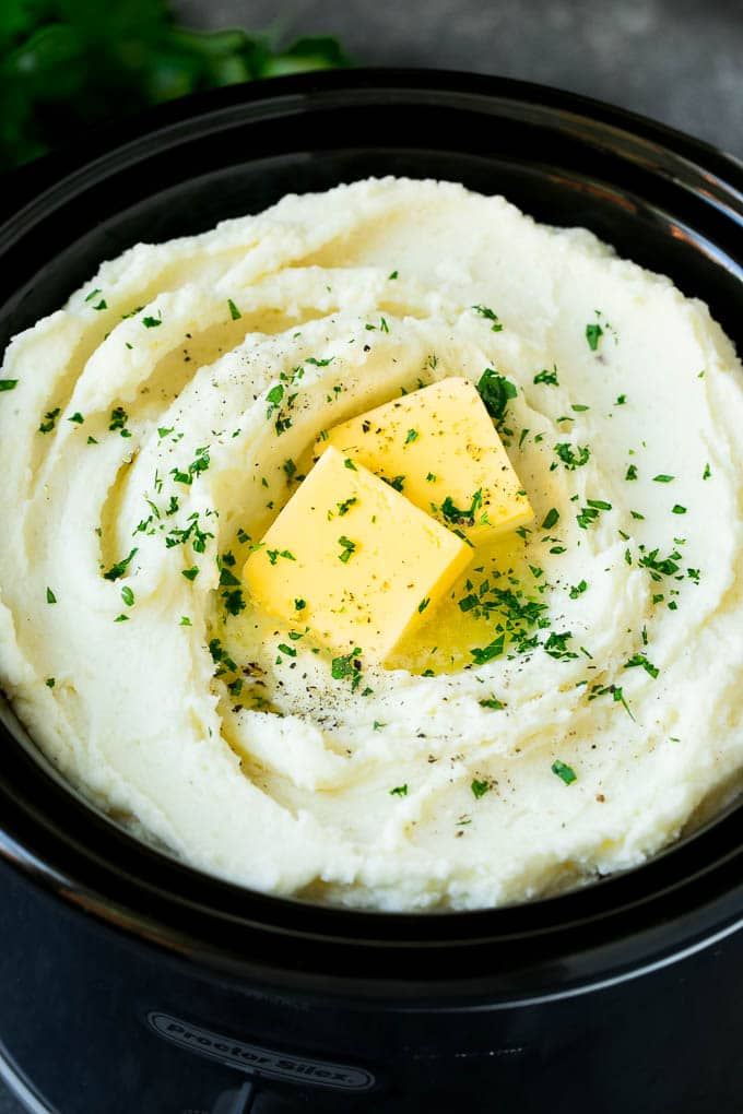 Crock pot mashed potatoes topped with pats of butter and parsley.