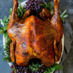 A deep fried turkey garnished with grapes and fresh herbs.