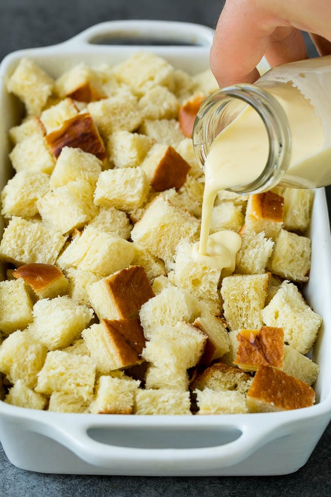 A mixture of milk and eggs being poured over cubes of bread.