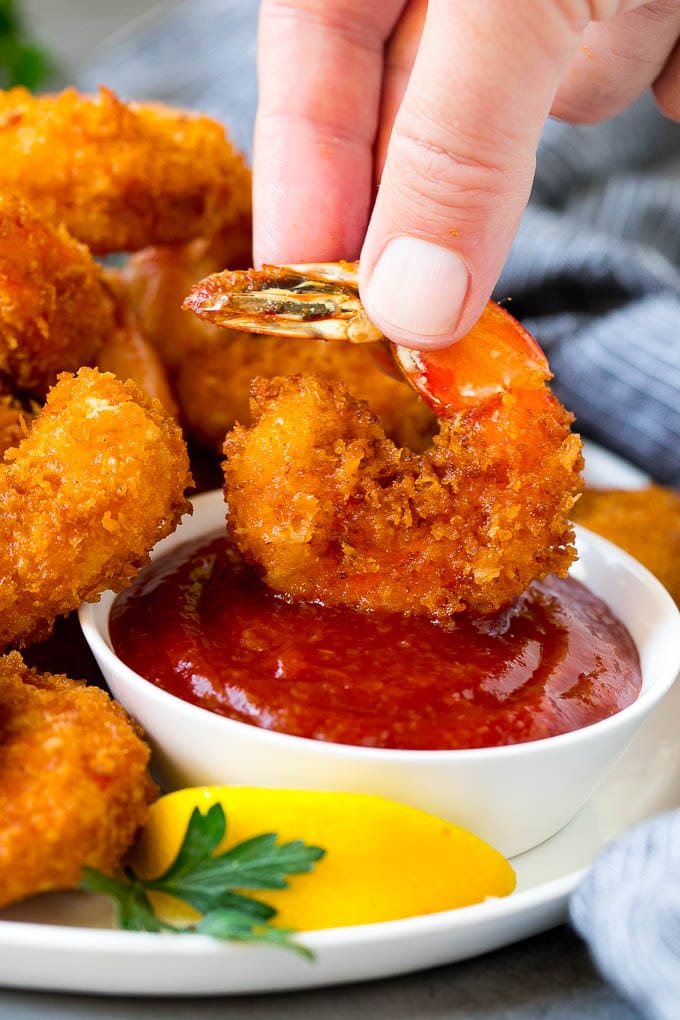 A hand dipping a shrimp into cocktail sauce.