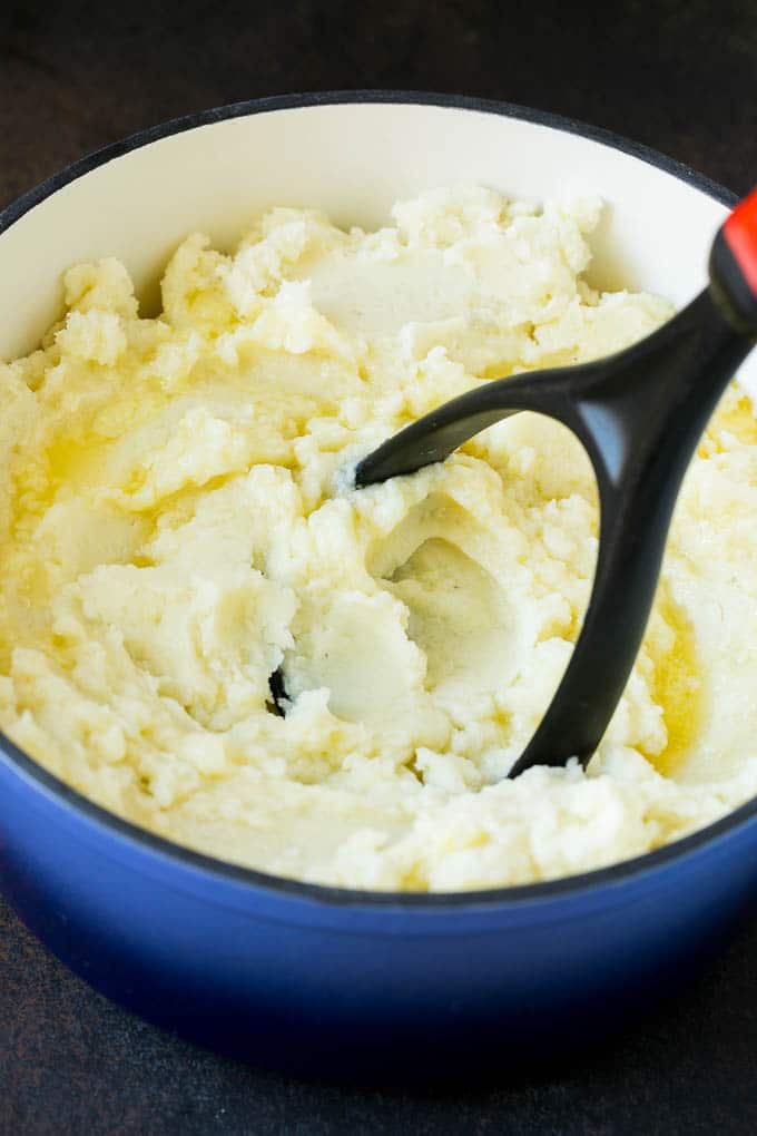 A potato masher smashing diced cooked potatoes.