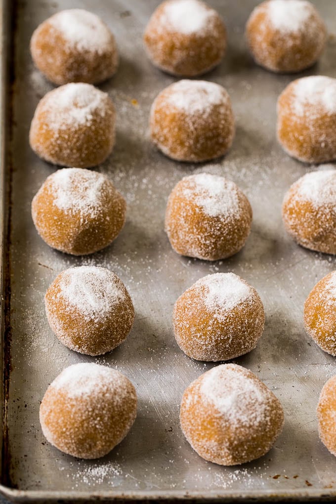 Balls of cookie dough rolled in sugar on a sheet pan.