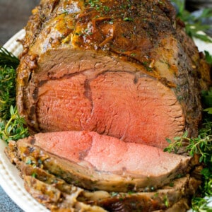 A sliced prime rib roast surrounded by fresh herbs.