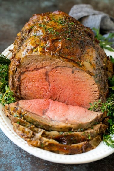 A sliced prime rib roast surrounded by fresh herbs.