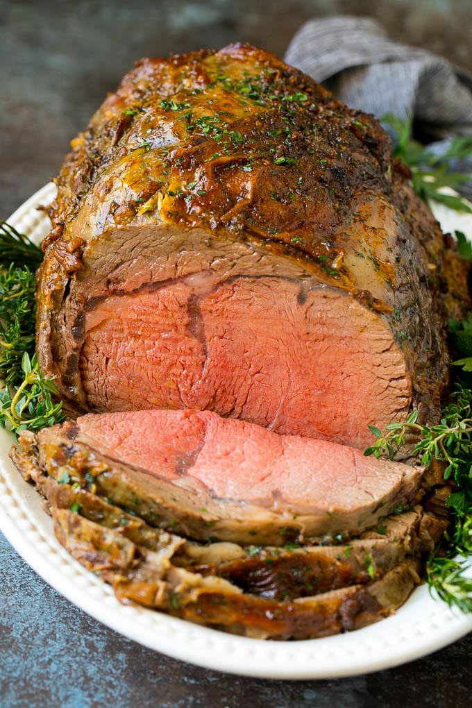 A sliced slow roasted prime rib roast surrounded by fresh herbs.